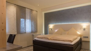 A modern bedroom with a large bed, bedside lamps, and a view of the city through a window with a curtain. - Ziegenbruch's Hotel & Restaurant (Spenge)