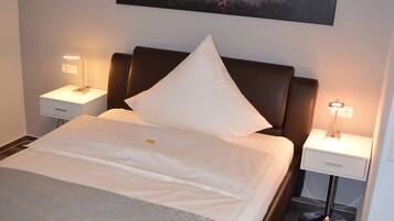 A neatly made bed with a pillow, a bedside table with a lamp, and a wall-mounted painting of a car.