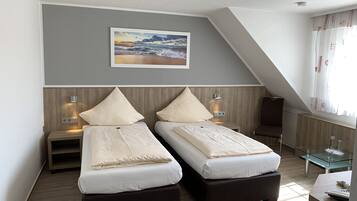 A hotel room with two beds, a wooden headboard, a painting of a beach scene, a glass table, and a window with curtains.