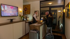 A hotel reception area with a wooden reception desk, a television displaying a welcome message, and a framed certificate on the wall. - Ziegenbruch's Hotel & Restaurant (Spenge)