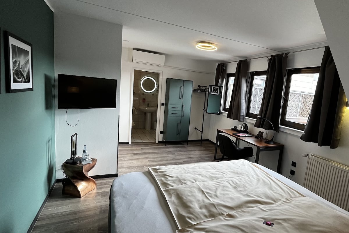 Une chambre d’hôtel avec un lit, un bureau, une chaise, une télévision et une salle de bain visible à travers une porte ouverte.