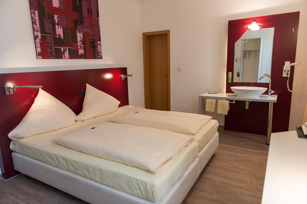 Une chambre d’hôtel avec un lit double, une table de chevet, un miroir, un lavabo et un mur d’accent de couleur rouge.