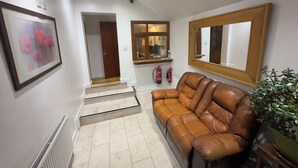 A hallway with a brown leather sofa, a framed picture, a mirror, a fire extinguisher, and a potted plant. - Dharma Lodge (Enfield)