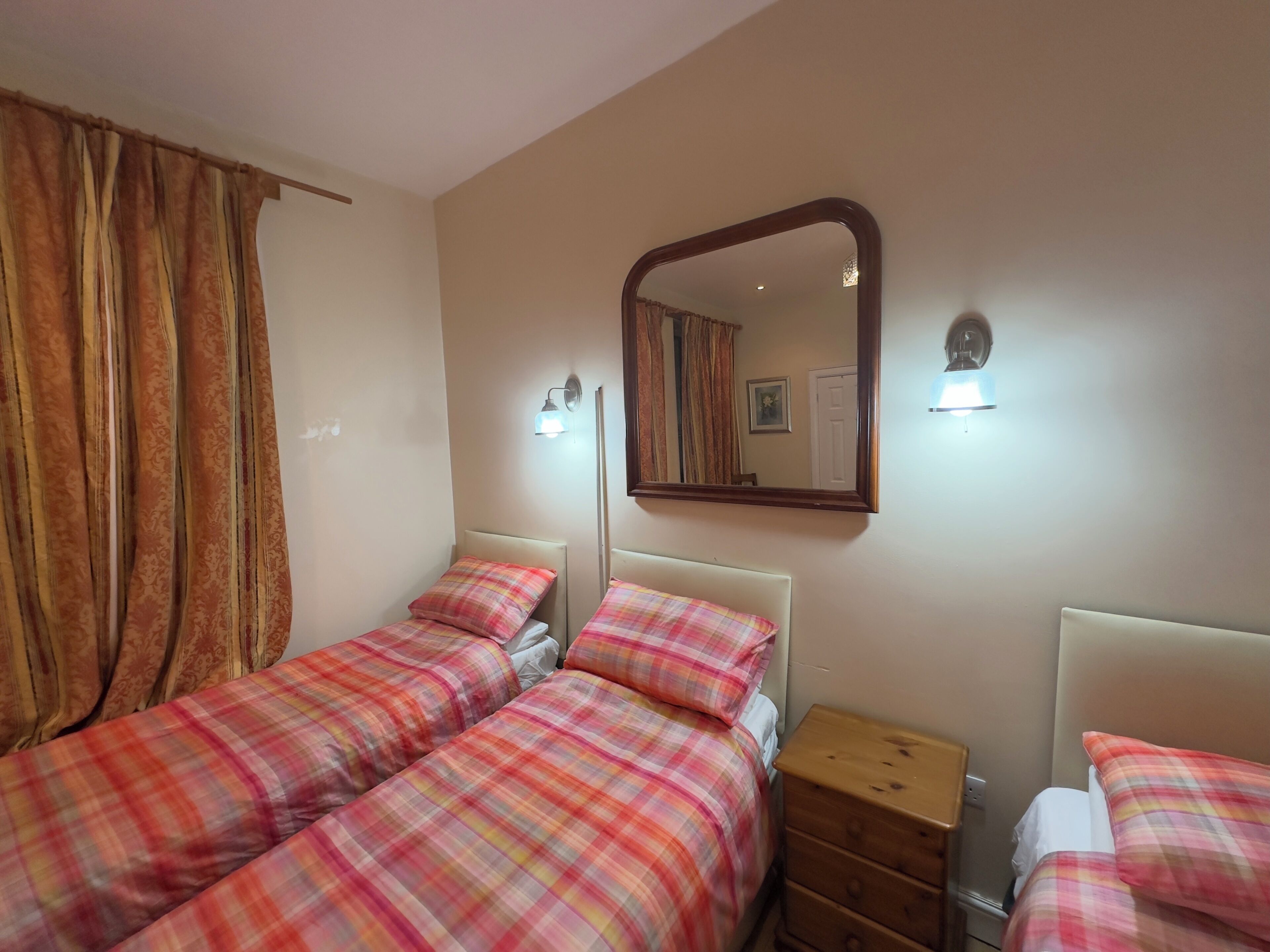 Una camera da letto con due letti, una cassettiera, uno specchio e un punto luce a parete.