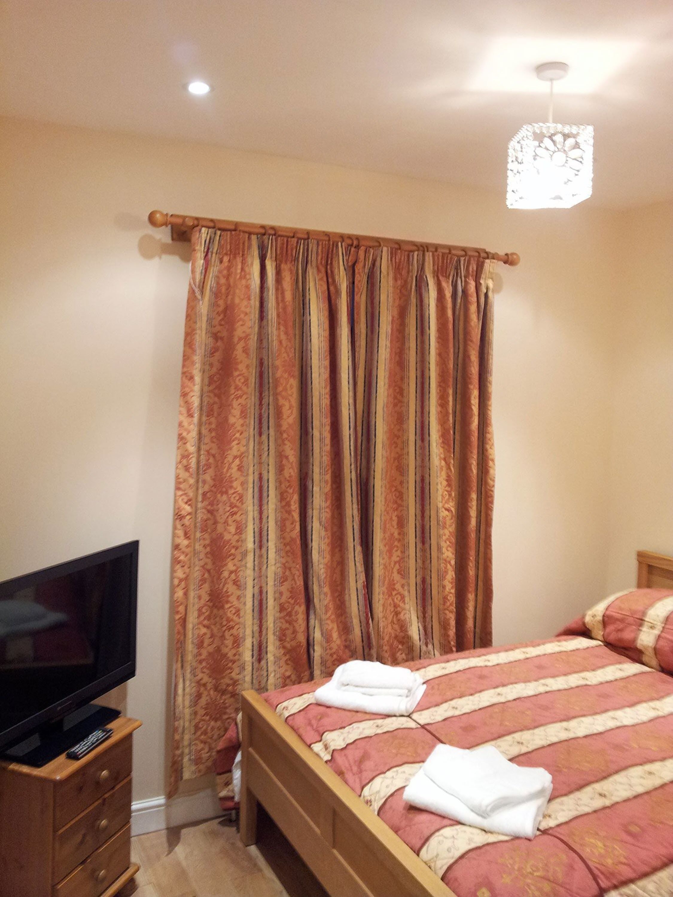 Quarto com cama, televisão sobre uma cômoda de madeira e cortina.