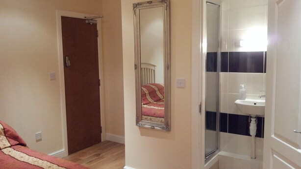 A bedroom with a bed, a bedside table, a mirror, and a bathroom with a sink and toilet. - Dharma Lodge (Enfield)