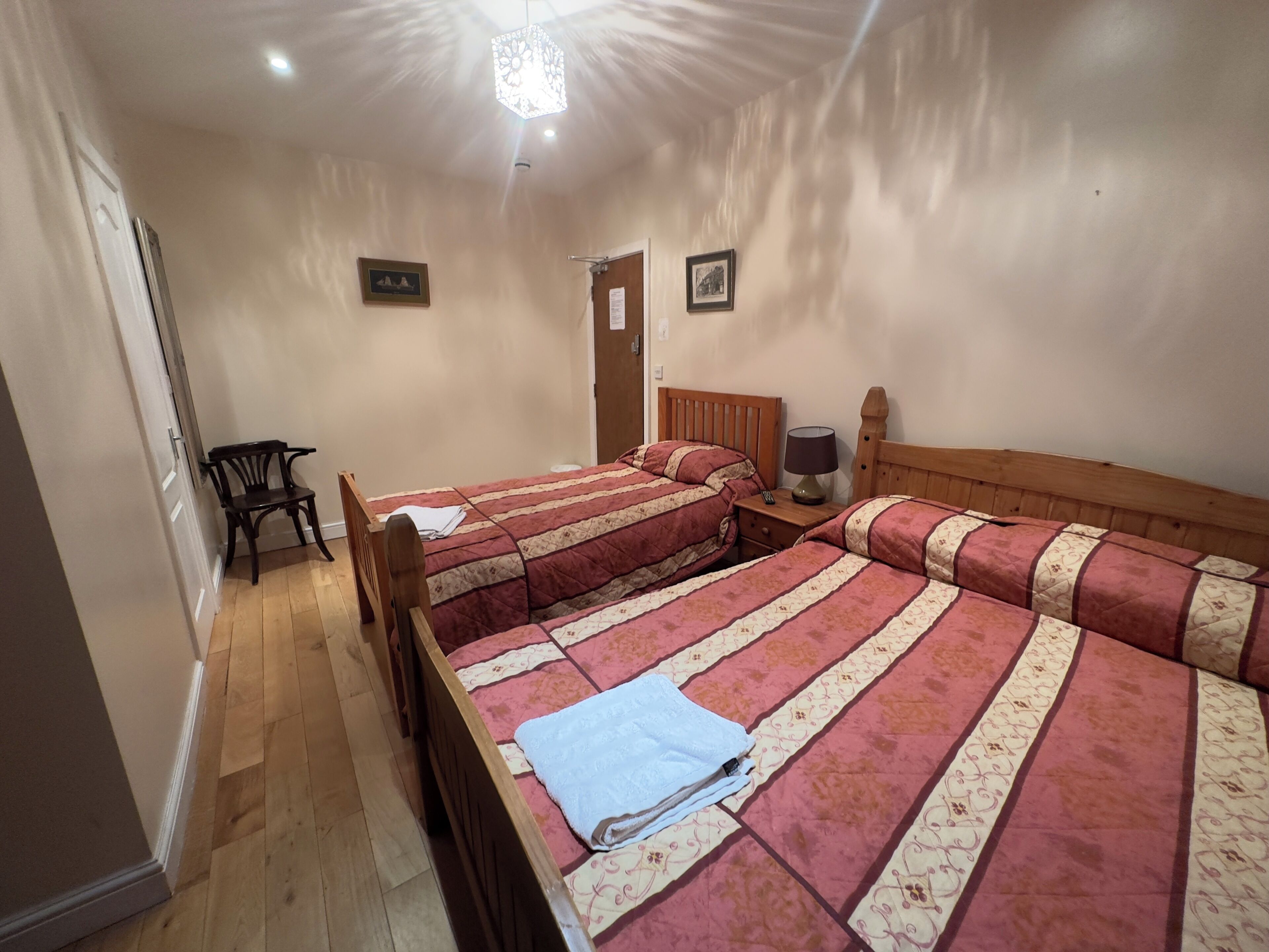 A bedroom with two beds, a wooden chair, a nightstand with a lamp, and a door.