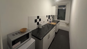 A compact kitchen with a microwave, a sink, and a window. - Dharma Lodge (Enfield)