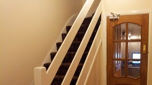 A staircase with white railings and dark carpeted steps leading to a wooden door with glass panels. - Dharma Lodge (Enfield)