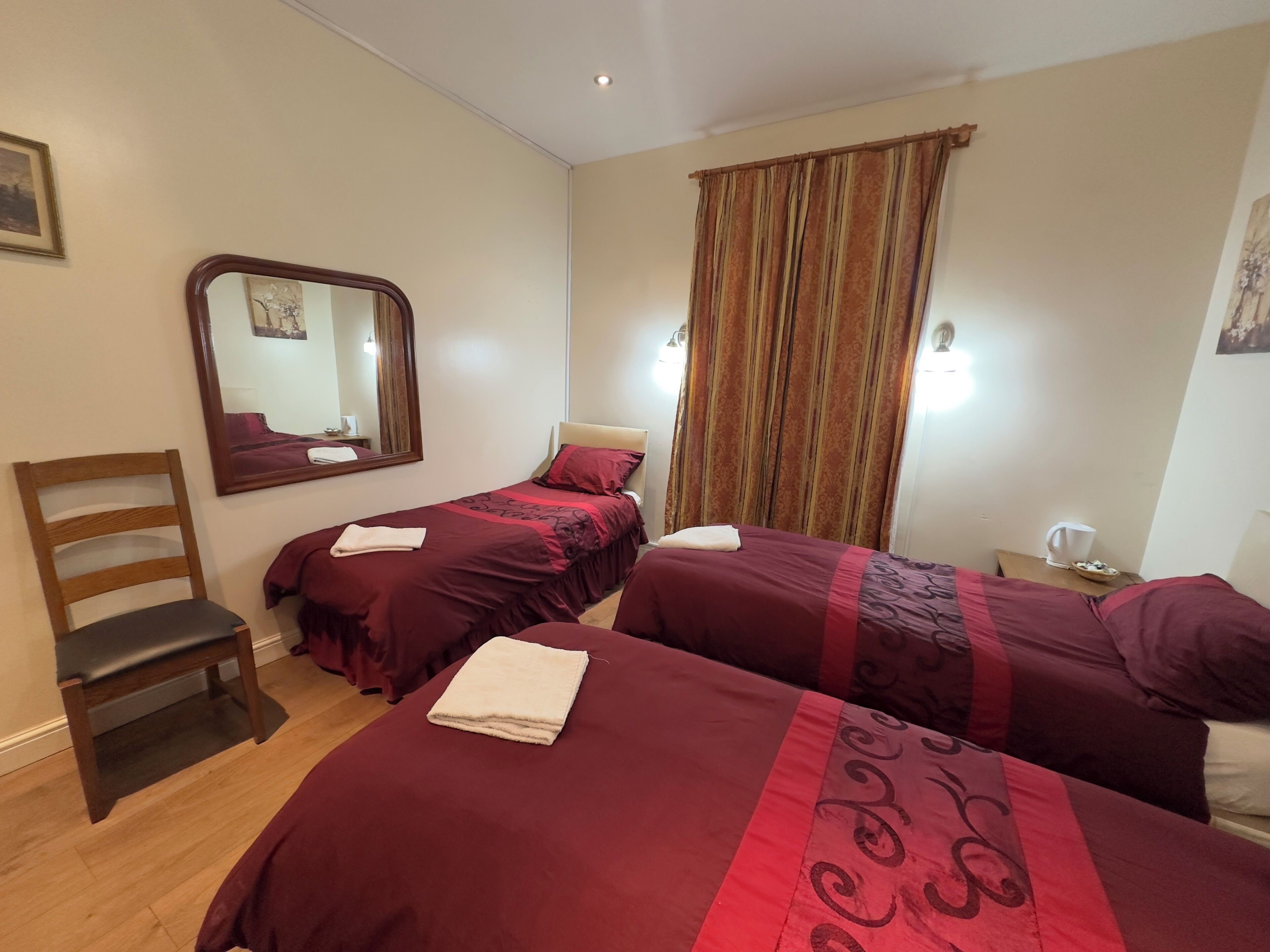 Habitación de hotel con dos camas, una silla de madera, un espejo y una mesita de noche con una taza.