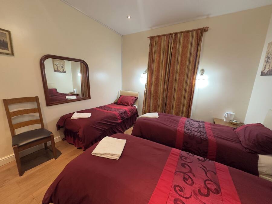 Une chambre d’hôtel avec deux lits, une chaise en bois, un miroir et une table de chevet avec une tasse.