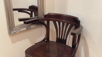 A wooden chair with a high backrest and a cushioned seat, positioned against a wall with a large mirror reflecting part of the room.