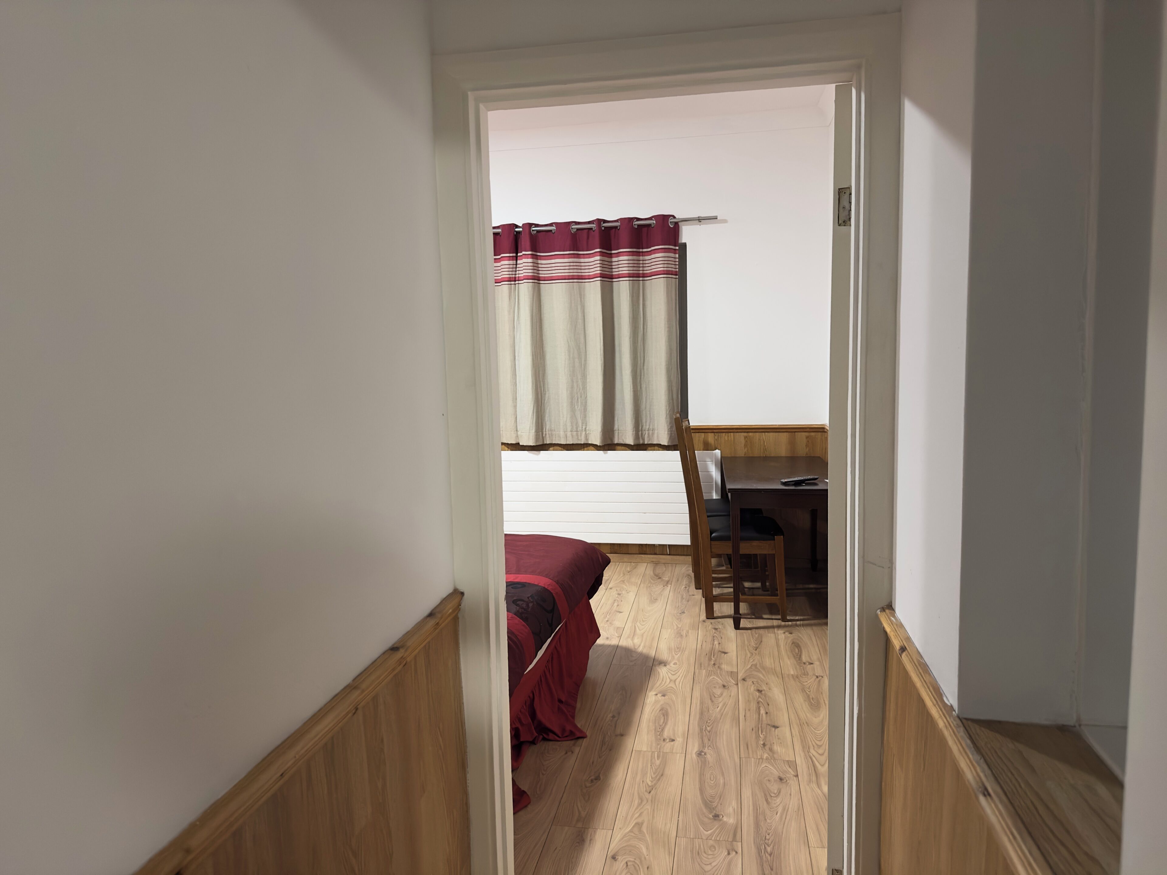 A narrow hallway leading to a bedroom with a bed, a desk, and a chair.