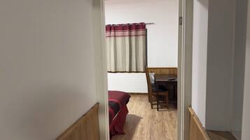 A narrow hallway leading to a bedroom with a bed, a desk, and a chair.