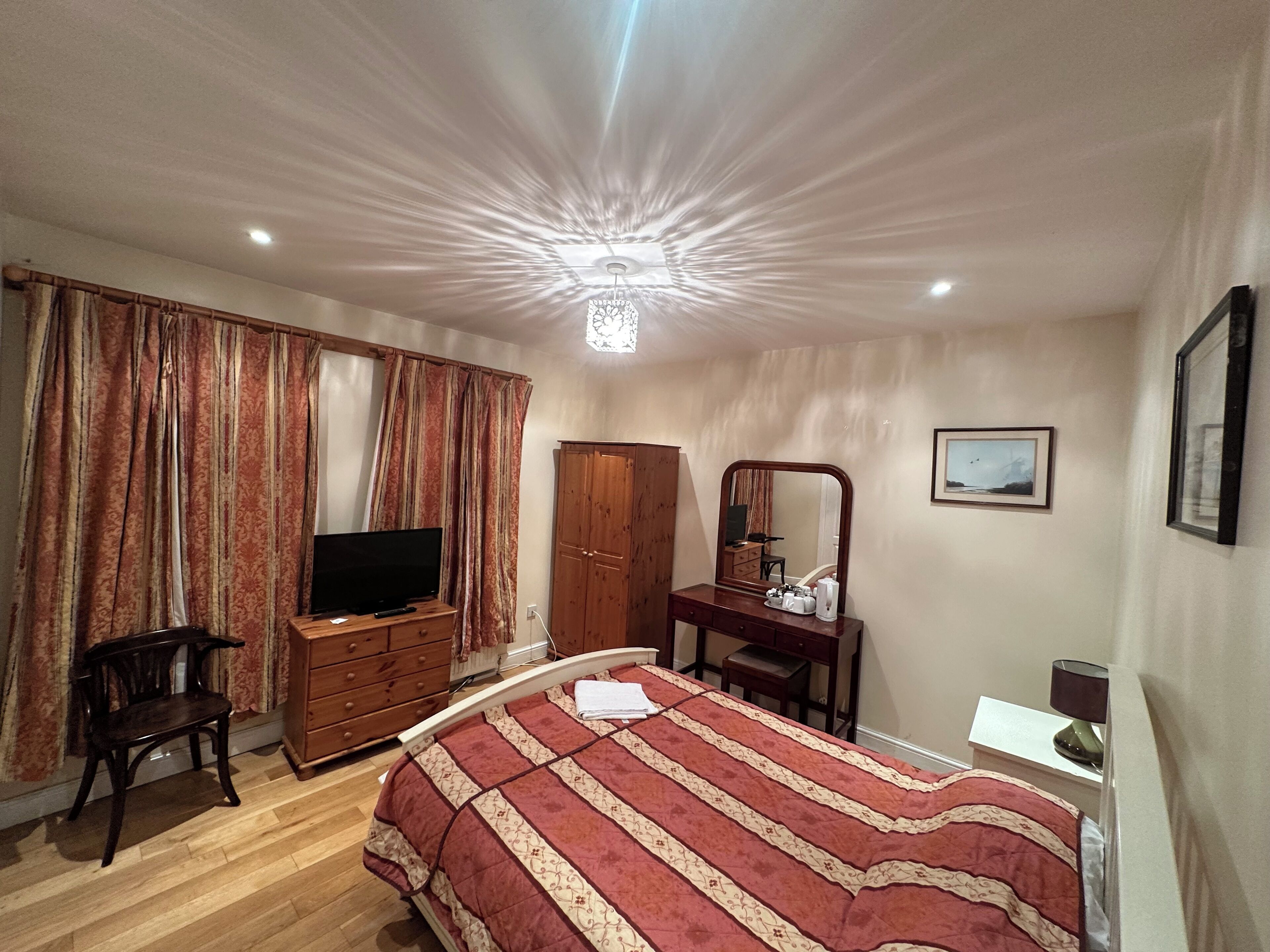 Un dormitorio con cama, televisión, armario, escritorio con espejo y un cuadro en la pared.