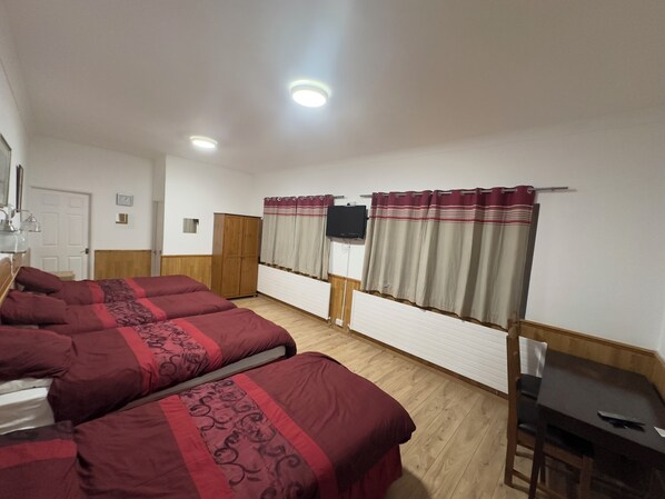 A room with two beds, a wooden wardrobe, a television on the wall, and a desk.
