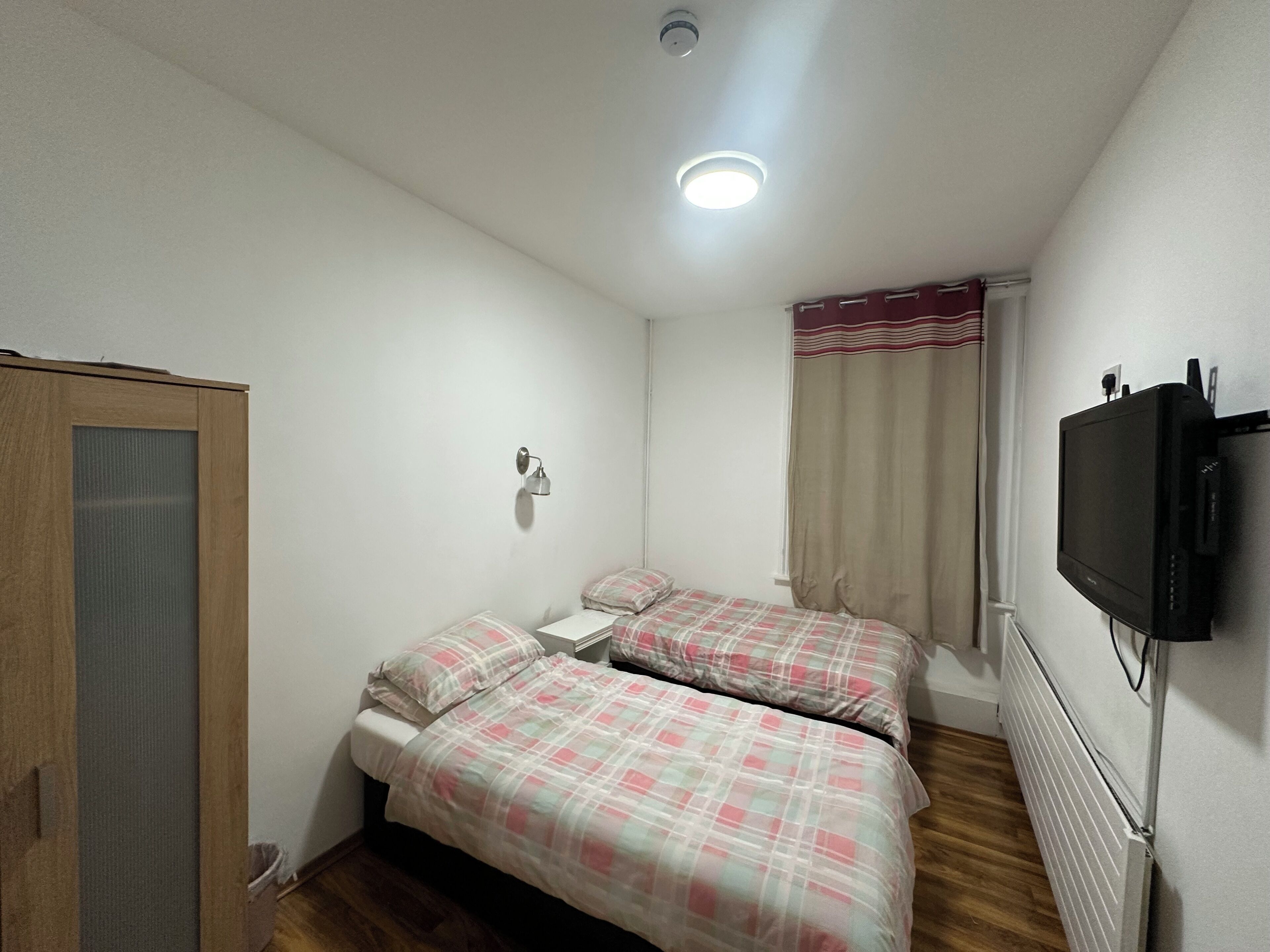 Ein Schlafzimmer mit zwei Betten, einem Fernseher, einem Fenster mit Vorhängen und einer Tür.