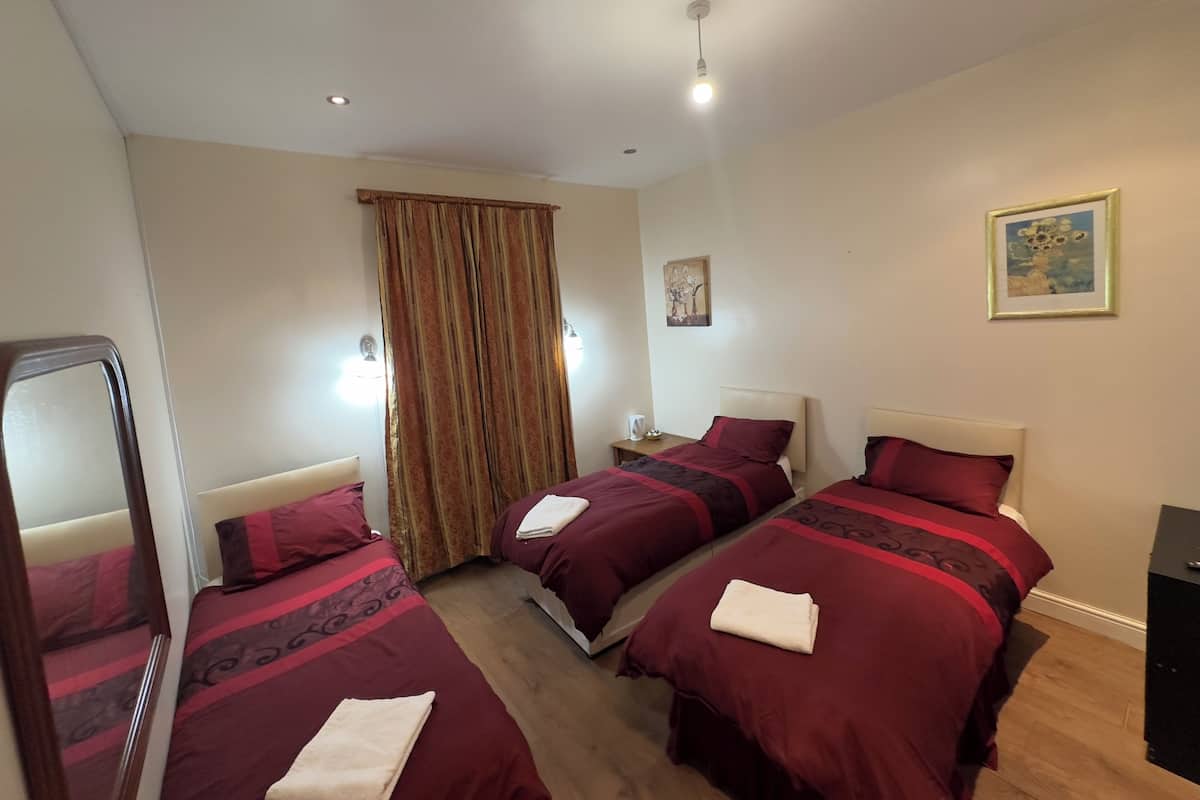 Quarto de hotel com duas camas, um espelho, uma janela com cortinas, uma mesinha de cabeceira e um quadro na parede.