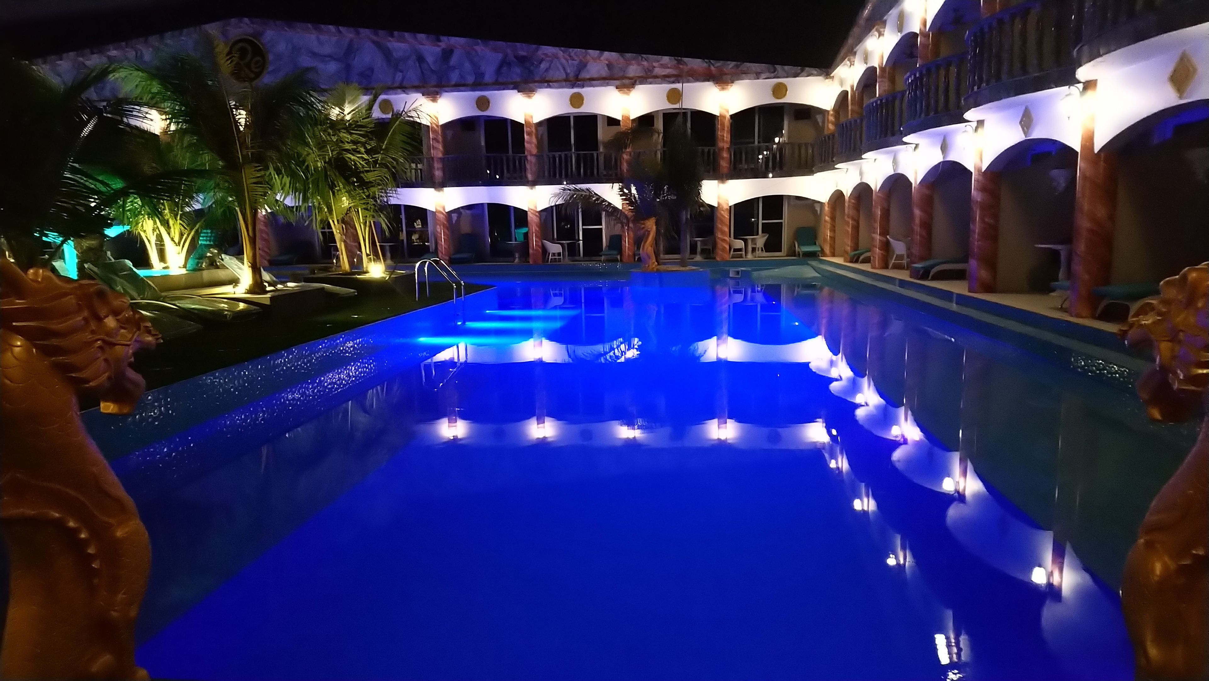 Una piscina con iluminación azul, rodeada por un edificio con varios balcones y arcos.