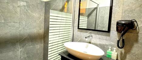A bathroom with a glass shower enclosure, a white sink, a black vanity, and a hairdryer mounted on the wall.