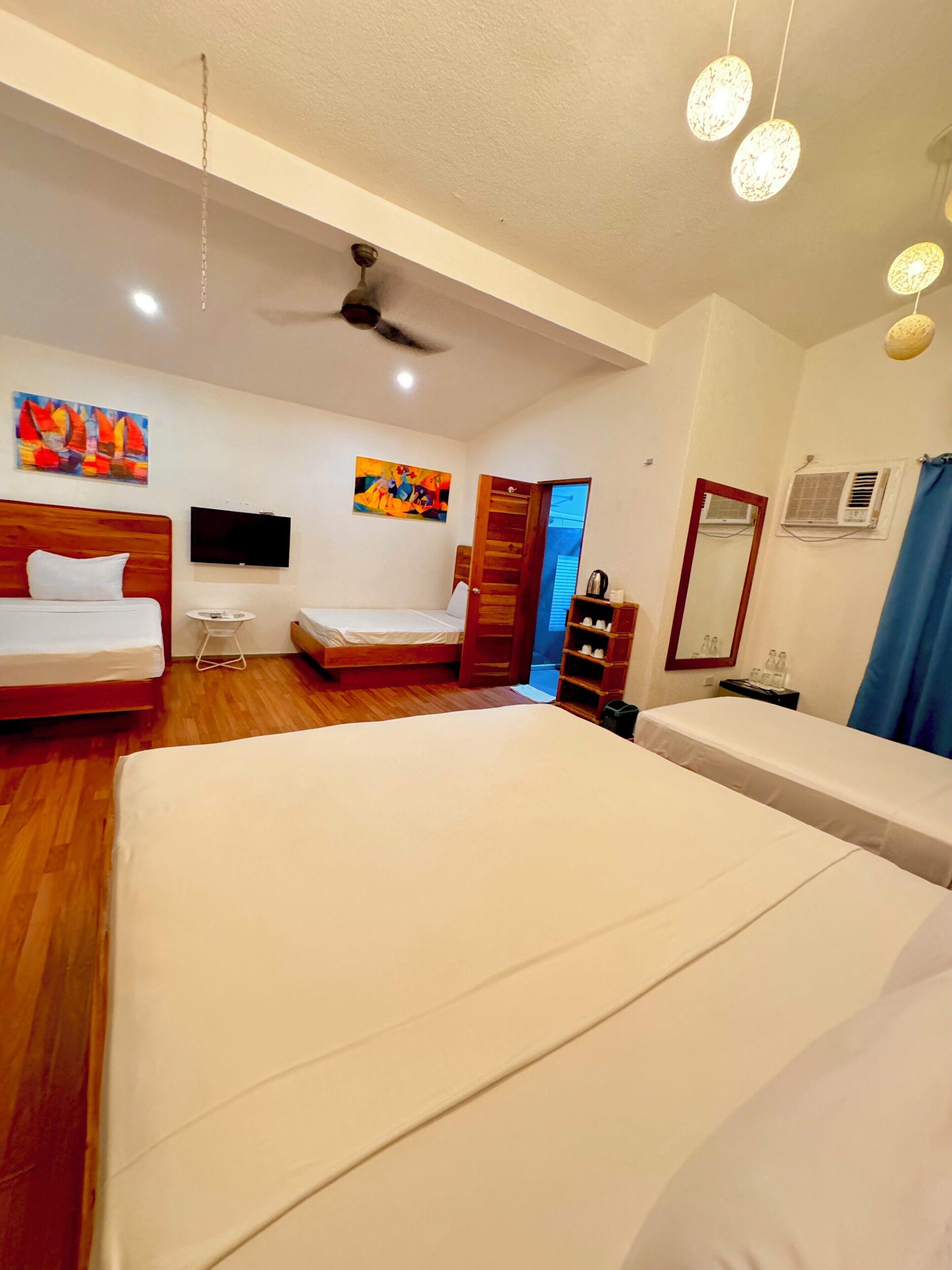 A hotel room with two beds, a ceiling fan, a TV, and artwork on the walls.