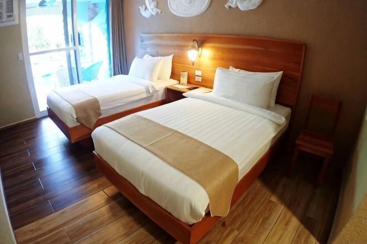 A hotel room with two beds, a wooden headboard, a nightstand, and a small table.