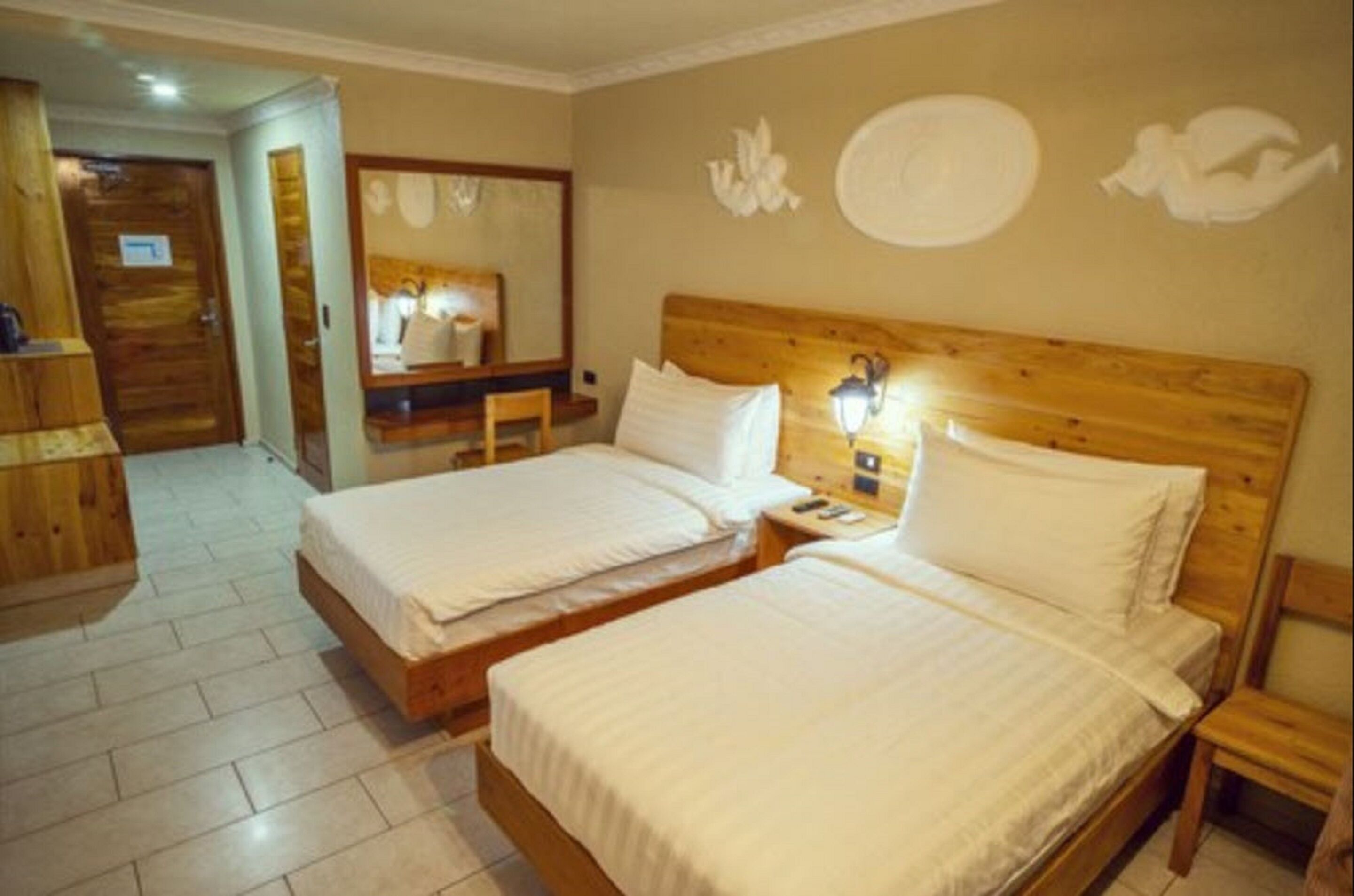 Une chambre d’hôtel avec deux lits, une tête de lit en bois, une table de chevet avec une lampe et un miroir au mur.