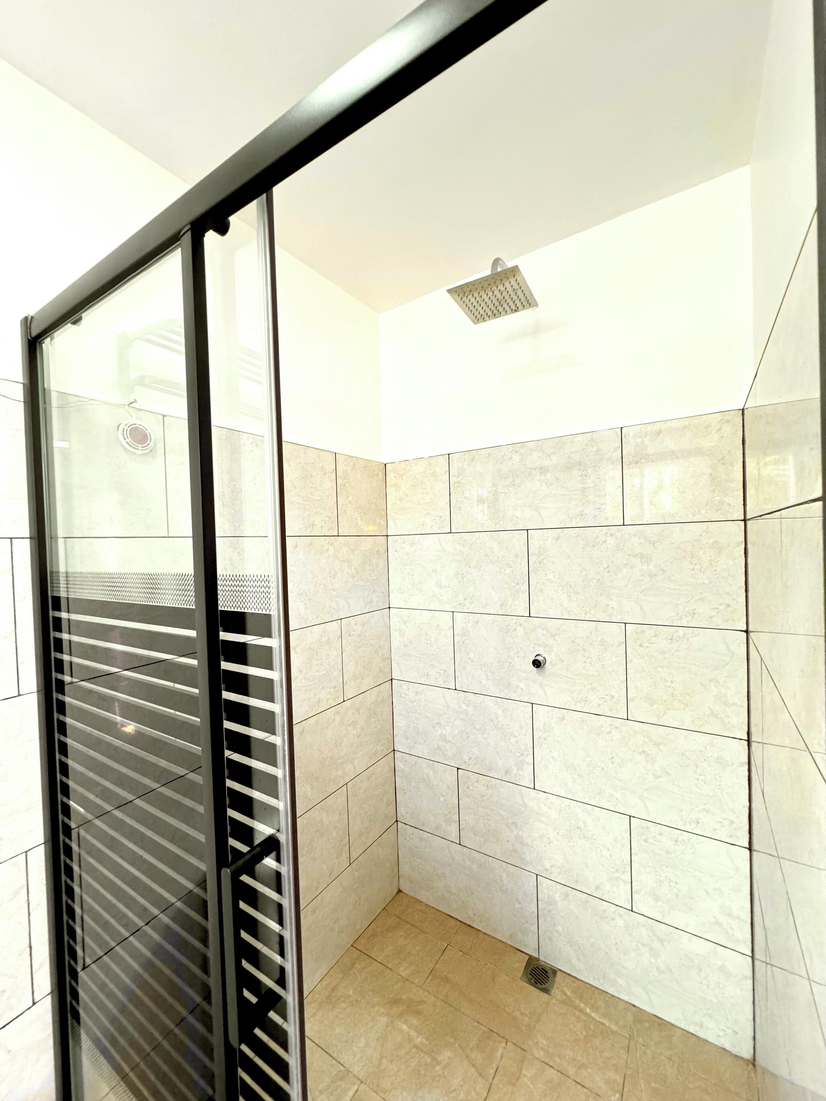 A shower with a glass door, tiled walls, and a ceiling-mounted showerhead.