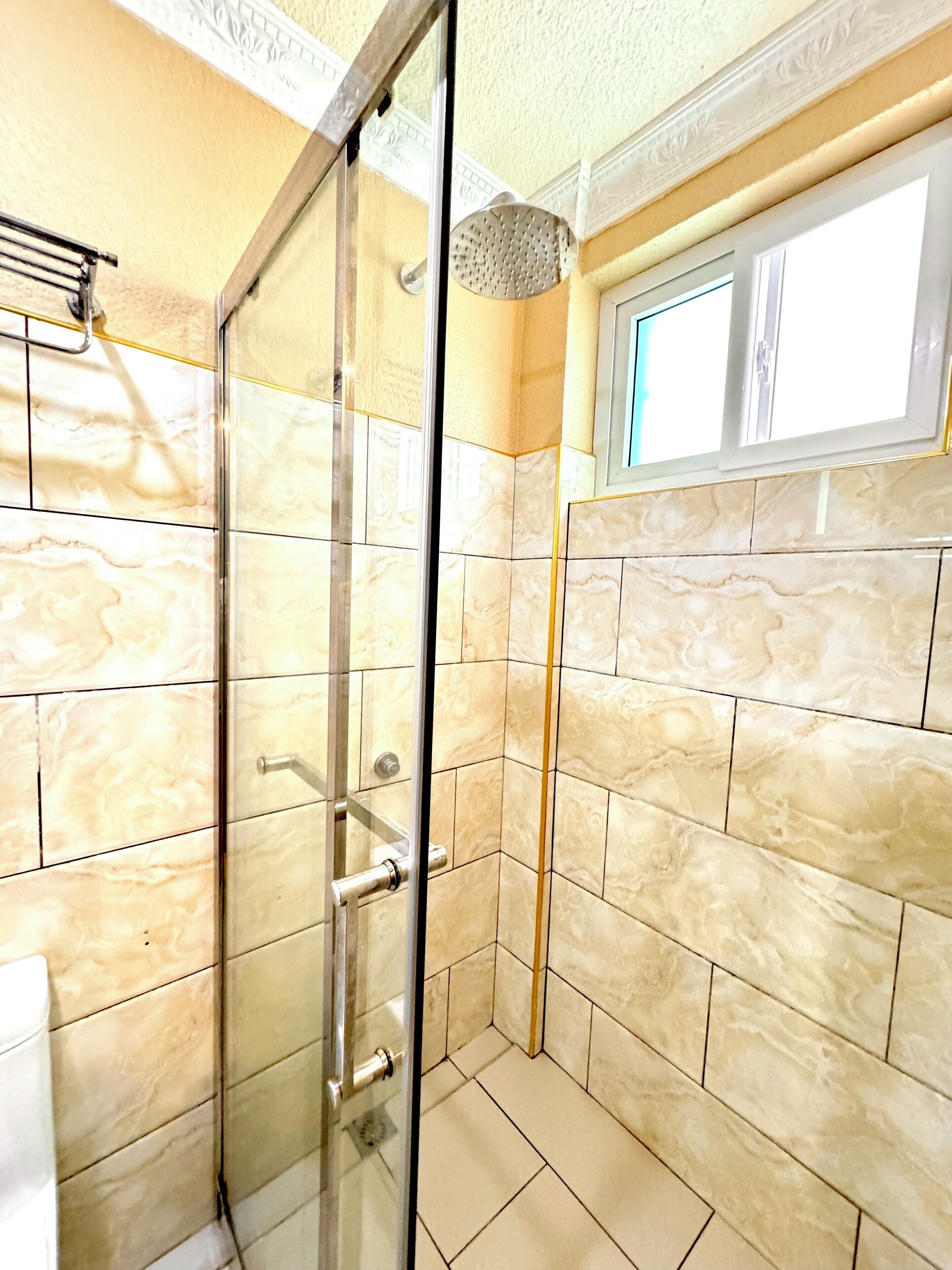 A glass-enclosed shower with marble tiles and a window above.