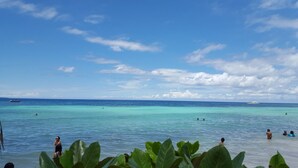 A beach with clear turquoise water, a few people swimming, and a boat in the distance.
