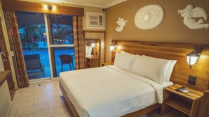 A hotel room with a large bed, wooden headboard, two bedside tables with lamps, a view through a glass door, and decorative wall art.