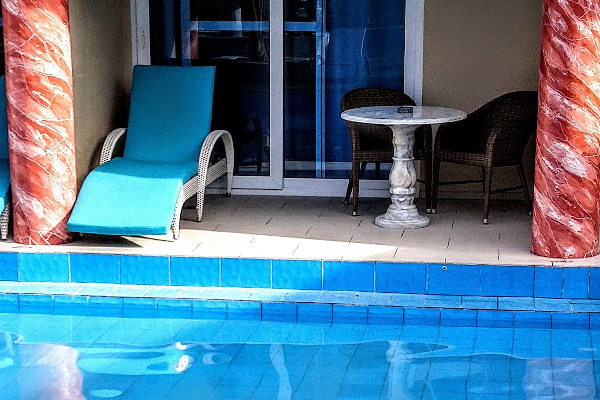A pool area with a lounge chair, a table, and a chair.