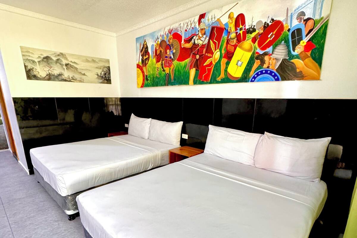 A hotel room with two beds, a large painting on the wall, and a window.