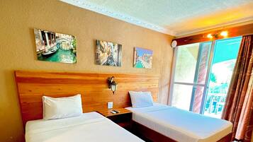 Quarto de hotel com duas camas, uma cabeceira de madeira, uma mesa de cabeceira, um abajur fixado na parede e três quadros emoldurados.