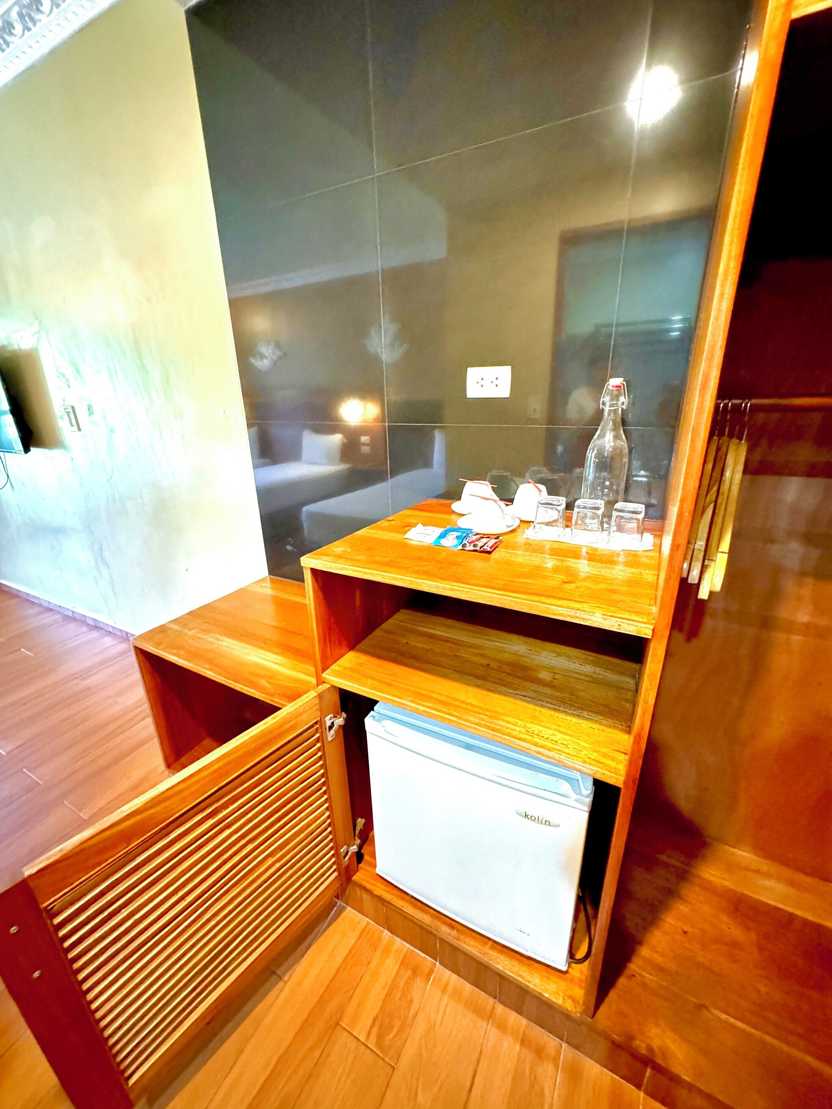 A compact kitchenette with a small refrigerator, wooden cabinets, and a countertop with various items.