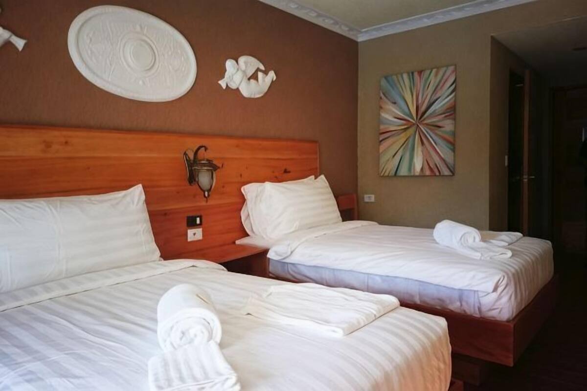 A hotel room with two beds, a wooden headboard, a wall-mounted lamp, and a colorful abstract painting.