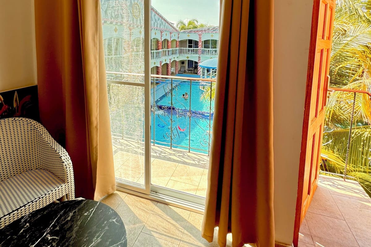 A room with a view of a swimming pool, a balcony with a railing, and a chair.