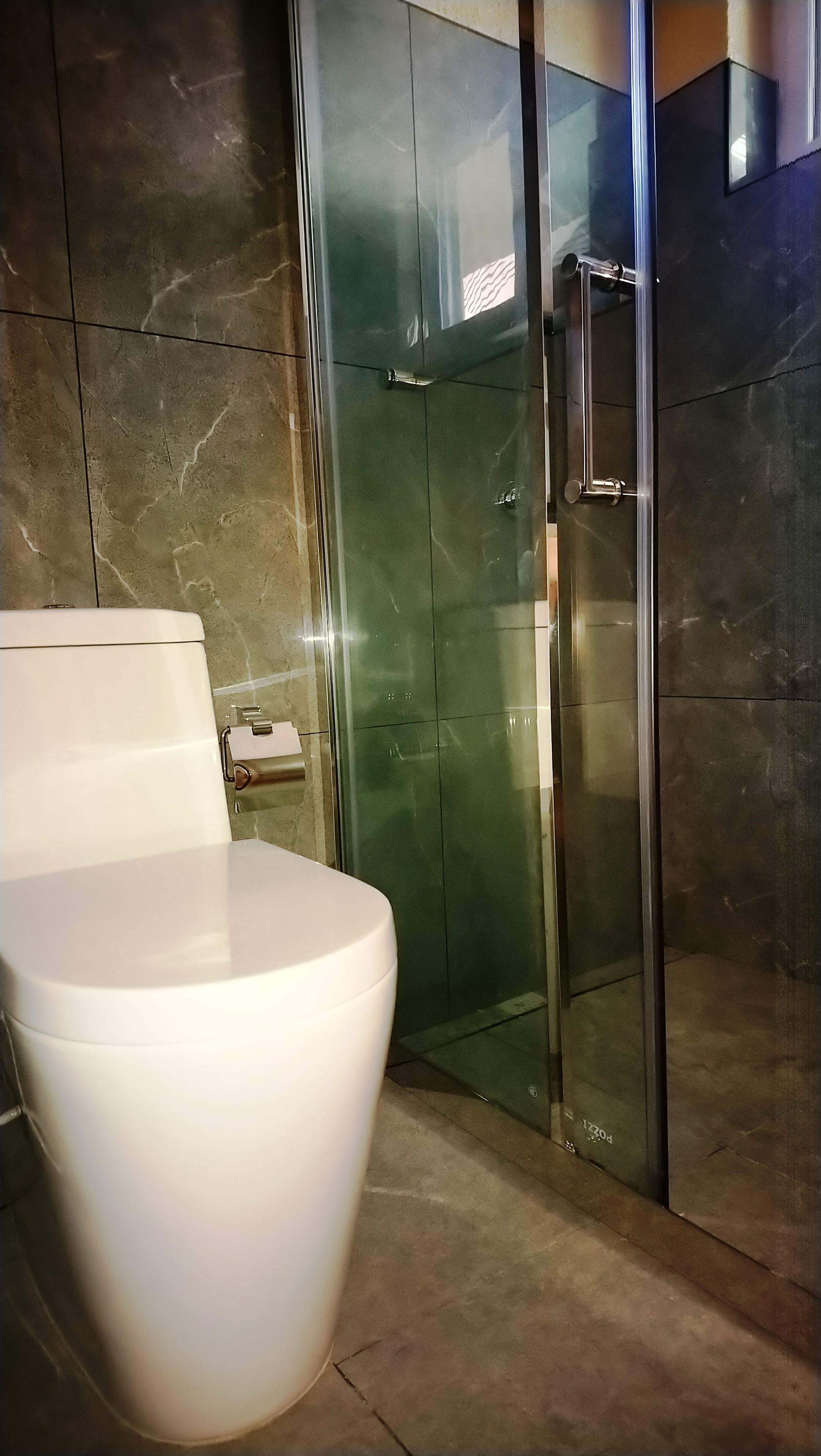 A modern bathroom with a toilet, a glass shower enclosure, and marble walls.
