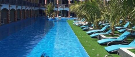 Una piscina con una persona nadando, rodeada de sillas de descanso y palmeras.