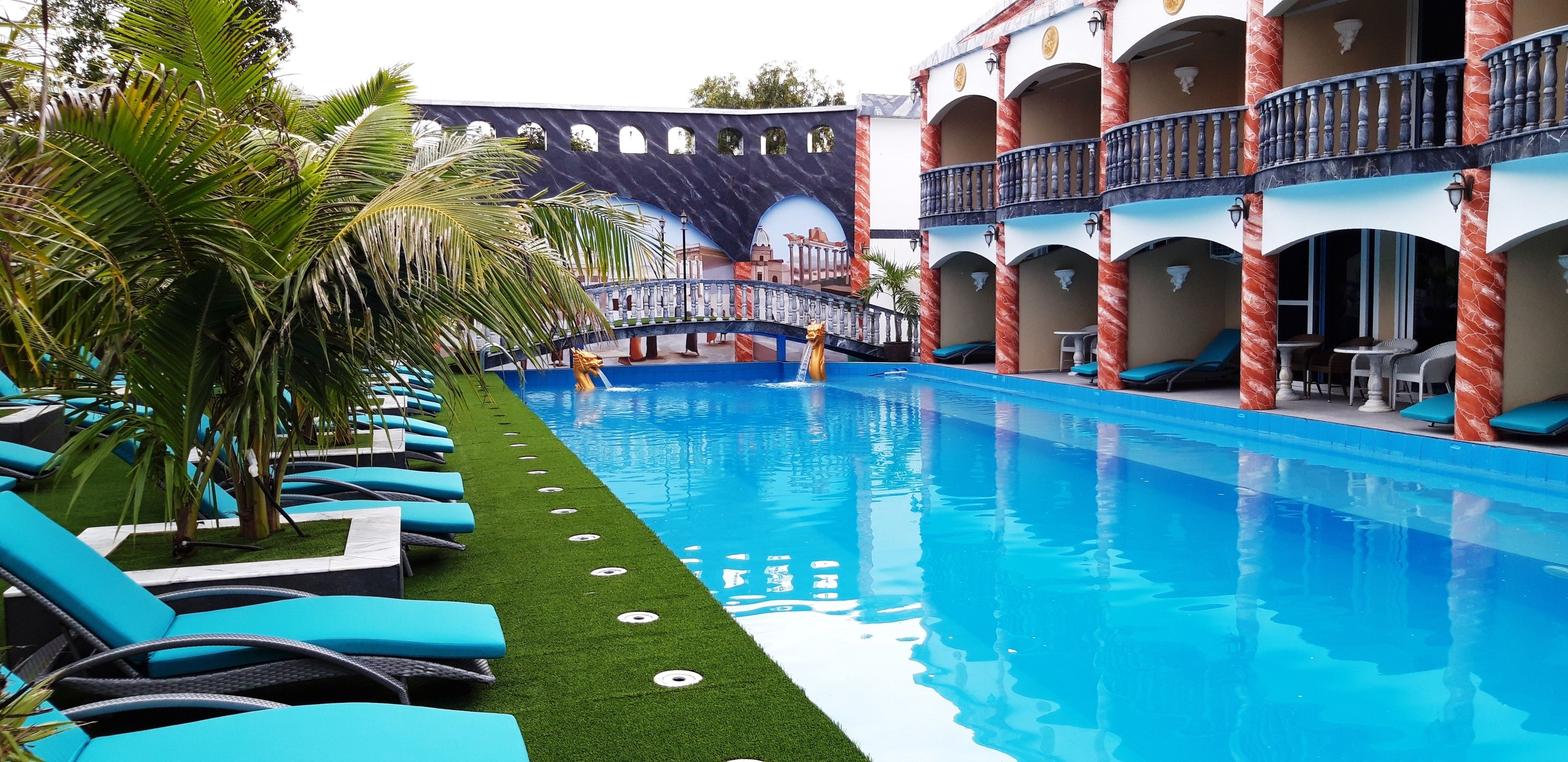 A swimming pool with blue water, surrounded by lounge chairs and palm trees.