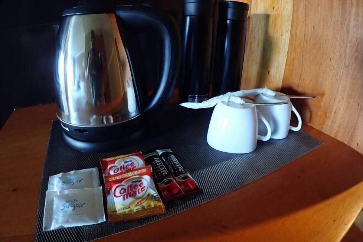A table with a coffee maker, white mugs, and coffee packets.