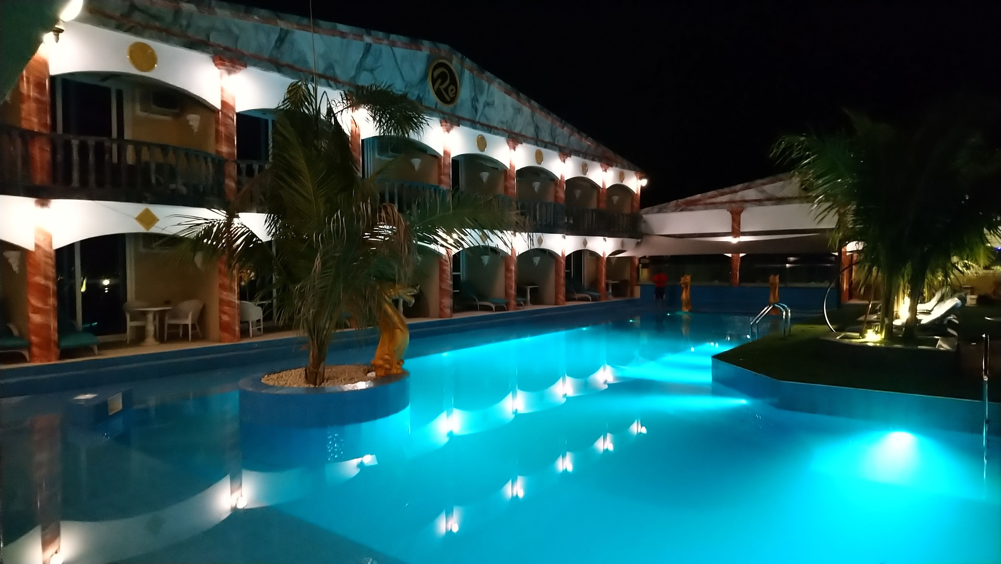 A swimming pool with a blue hue, surrounded by palm trees and lounge chairs.