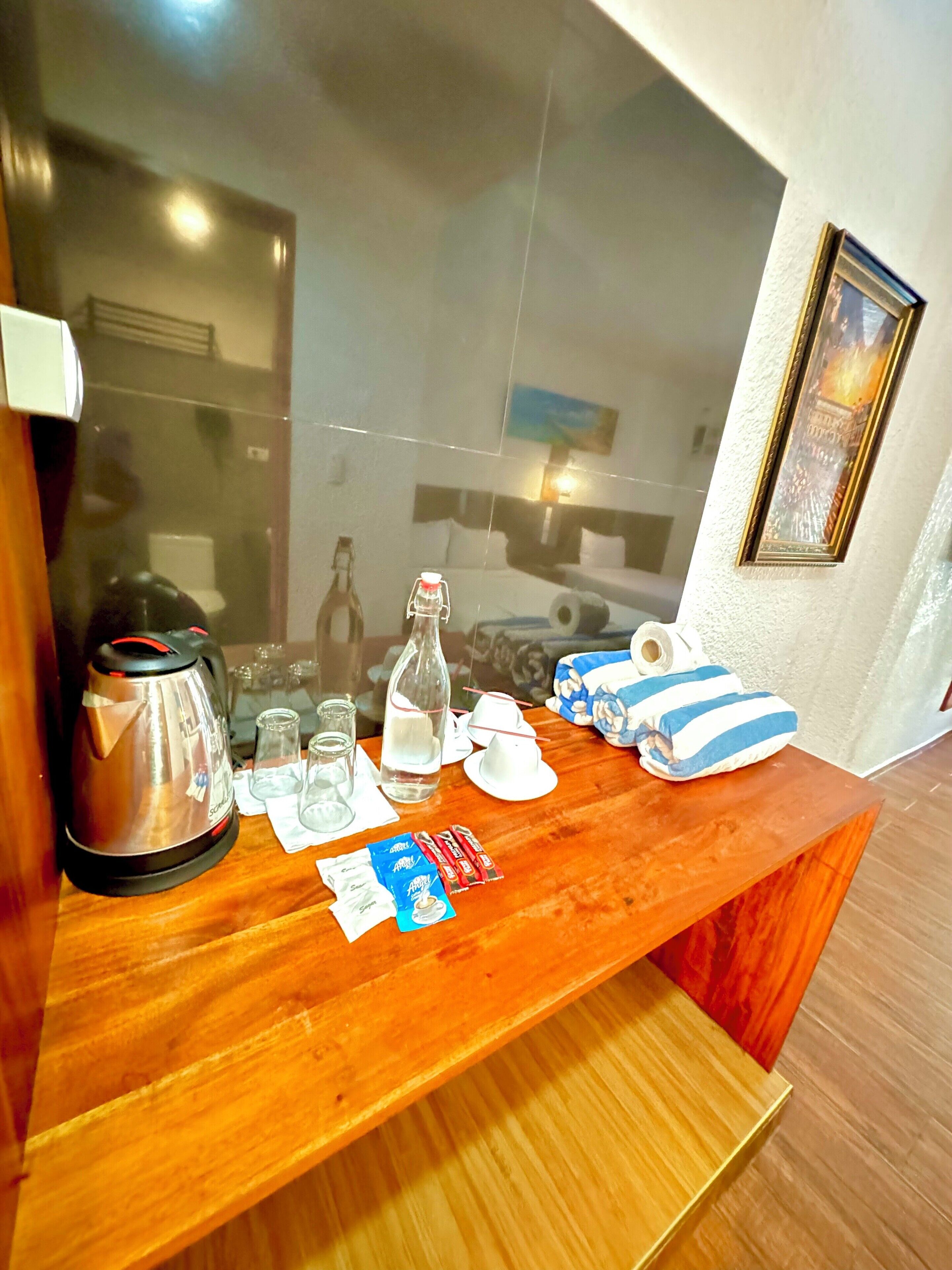 A wooden counter with a kettle, glasses, a bottle, and a pillow.