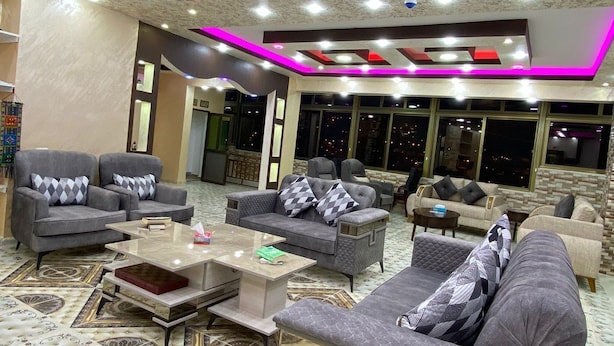 Eine großzügige Lounge mit mehreren Sofas und Sesseln, einem gemusterten Teppich sowie einer Decke mit Einbautenleuchten und Neonakzenten.