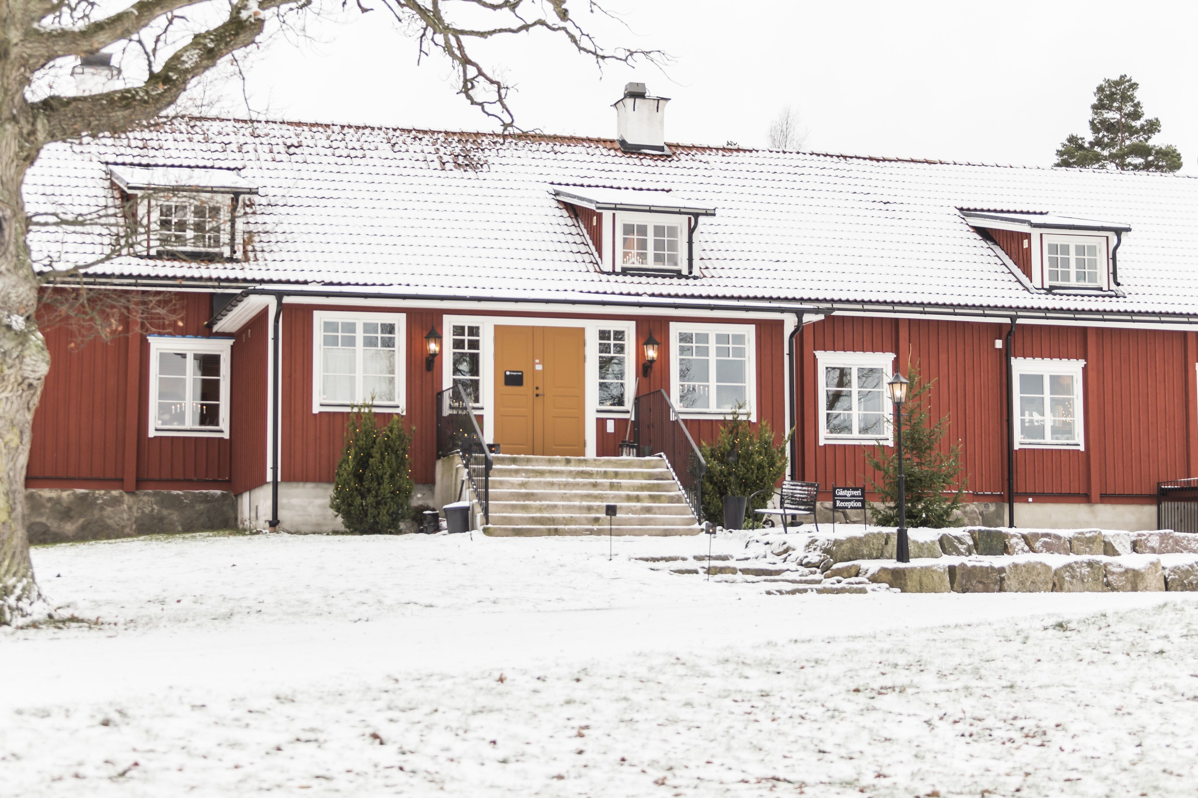Una casa di legno rossa con tetto innevato, una porta d'ingresso e una scala che conduce all'entrata.
