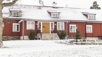 Una casa di legno rossa con tetto innevato, una porta d'ingresso e una scala che conduce all'entrata.