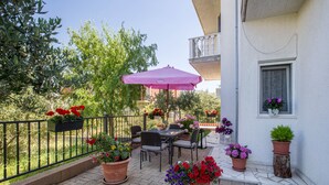 An outdoor patio with a table and chairs, surrounded by potted plants and a pink umbrella. - Apartments Toni Relax (Split)