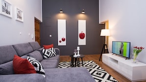 A modern living room with a grey sofa, red and black patterned pillows, a small round table with a white candle, and a flat-screen TV on a white stand. - Apartments Toni Relax (Split)