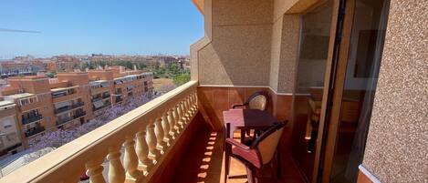 A balcony with a table and chairs, a view of surrounding buildings, and a door with a glass panel.