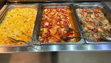 Un bufé con tres opciones: un guiso, pasta con vegetales y un plato de pollo con tomates.